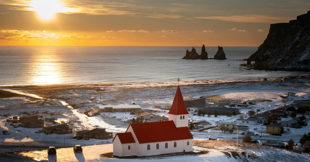 Sunset over the Icelandic coast with a red-roofed church and sea stacks