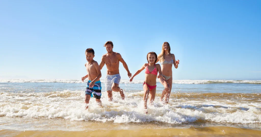 Family of four holding hands and running along the shore on a sunny beach