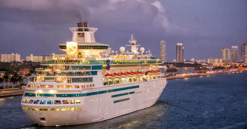 Large cruise ship docked in a port at dusk with city lights in the background