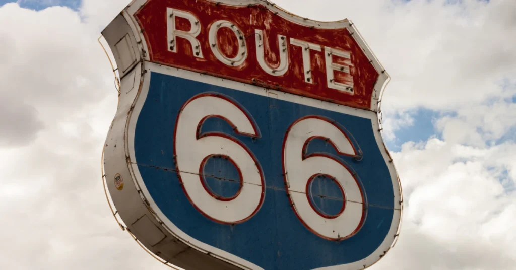 Blue Route 66 highway shield sign against a cloudy sky