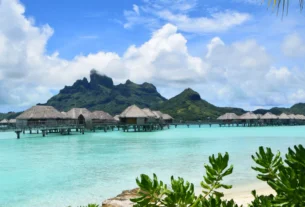 Overwater bungalows over turquoise lagoon with a mountain in the background