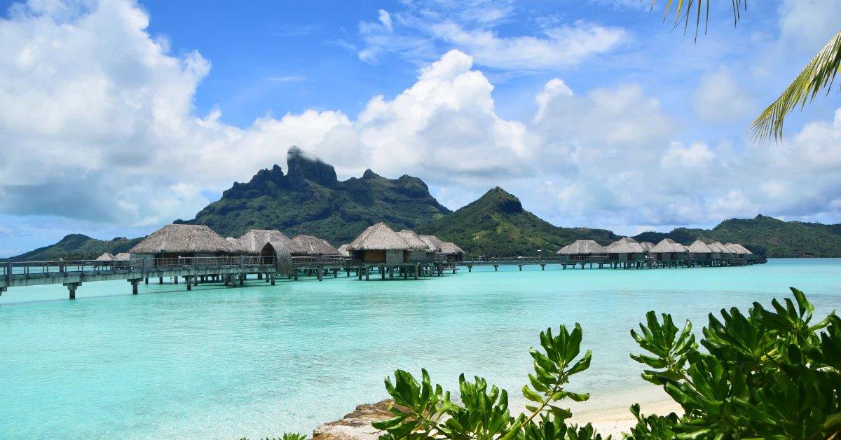 Overwater bungalows over turquoise lagoon with a mountain in the background