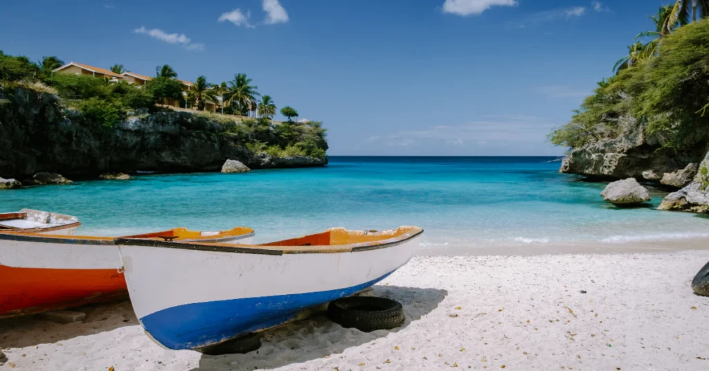 Small cove beach with turquoise water and a blue boat on the sand in Curaçao