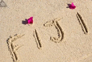 The word Fiji written in the sand on a beach with pink flowers