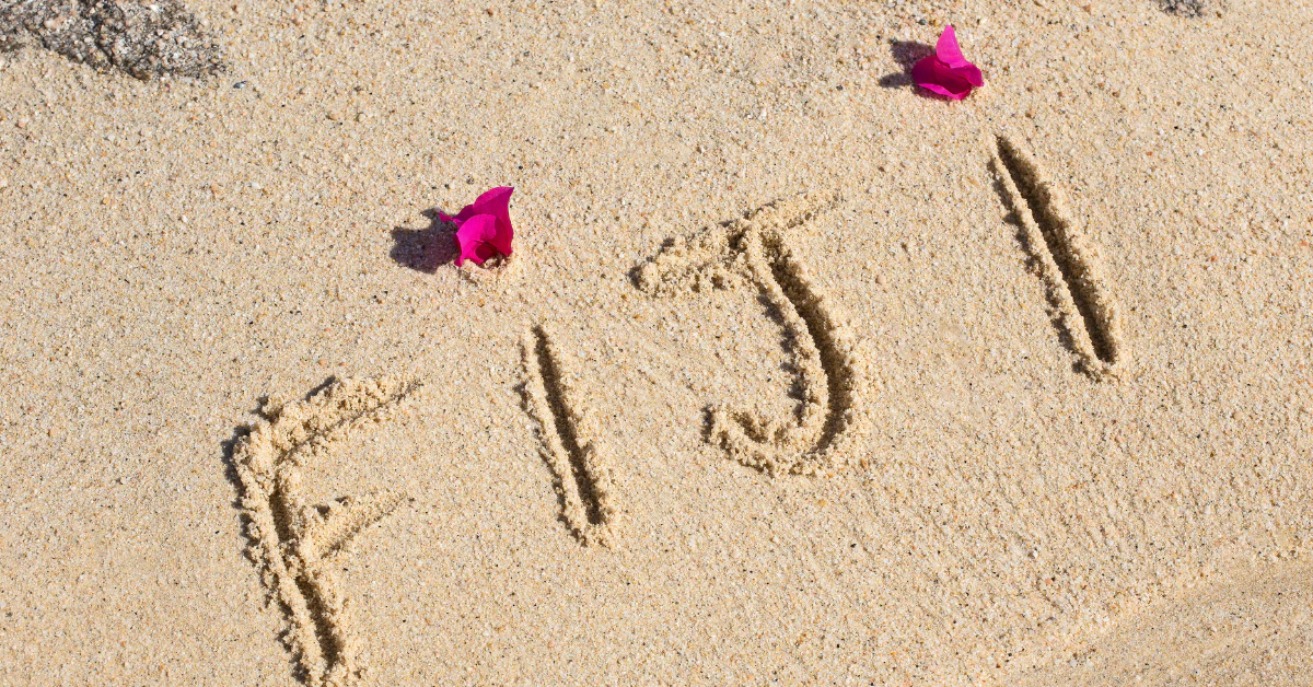 The word Fiji written in the sand on a beach with pink flowers