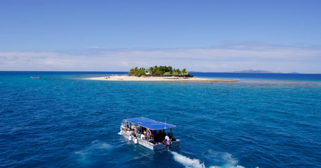 Boat traveling across blue water toward a small tropical island in Fiji