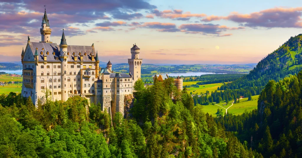 Neuschwanstein Castle surrounded by green forest and mountains in Bavaria at sunset