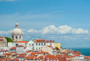 Red-roofed buildings and a domed church overlooking the river and sea under a blue sky