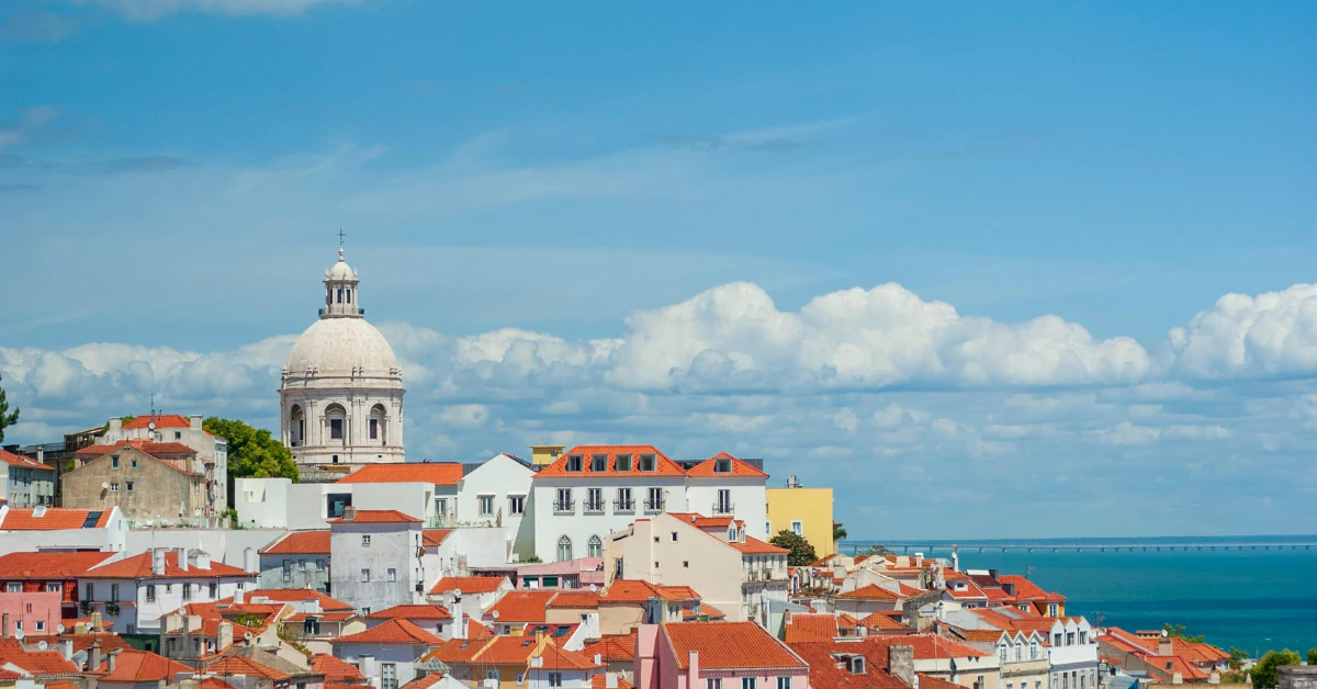 Red-roofed buildings and a domed church overlooking the river and sea under a blue sky
