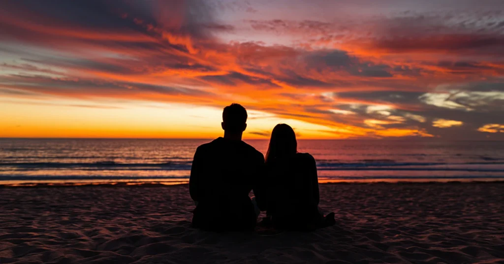 Couple sitting on a beach watching a colorful sunset