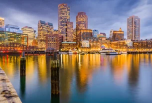 Boston skyline glowing at dusk with city lights reflecting on the harbor water